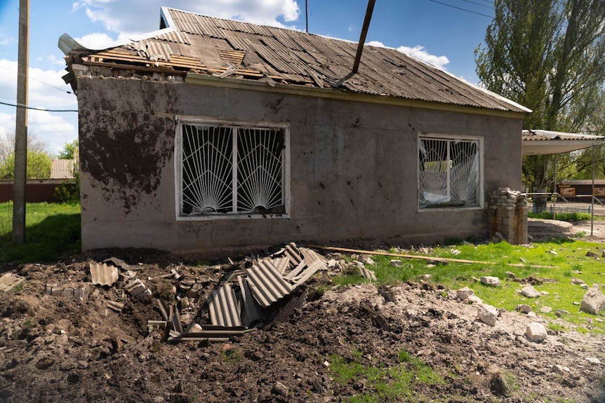 A broken down house with shattered windows and twisted metal in the front yard.