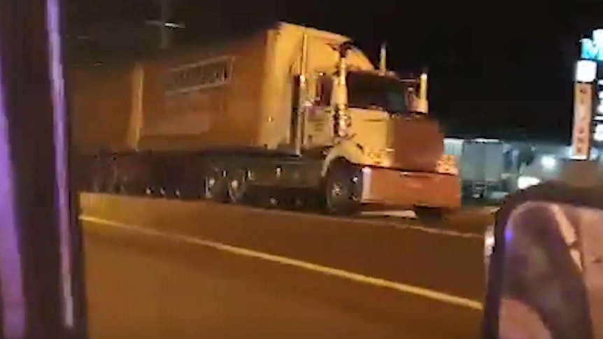 A video screengrab of double-carriage truck seen from the perspective of inside a car, driving down a road at night.
