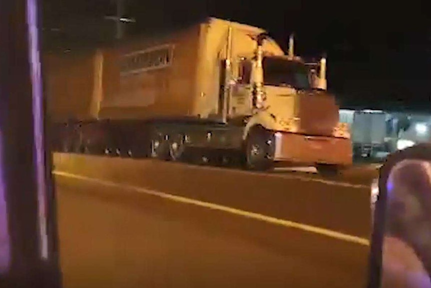 A video screengrab of double-carriage truck seen from the perspective of inside a car, driving down a road at night.