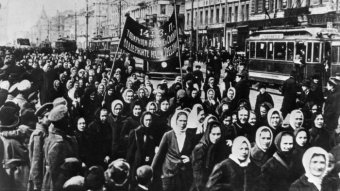 A black and white photo of women marching in the street with a banner in Russian.