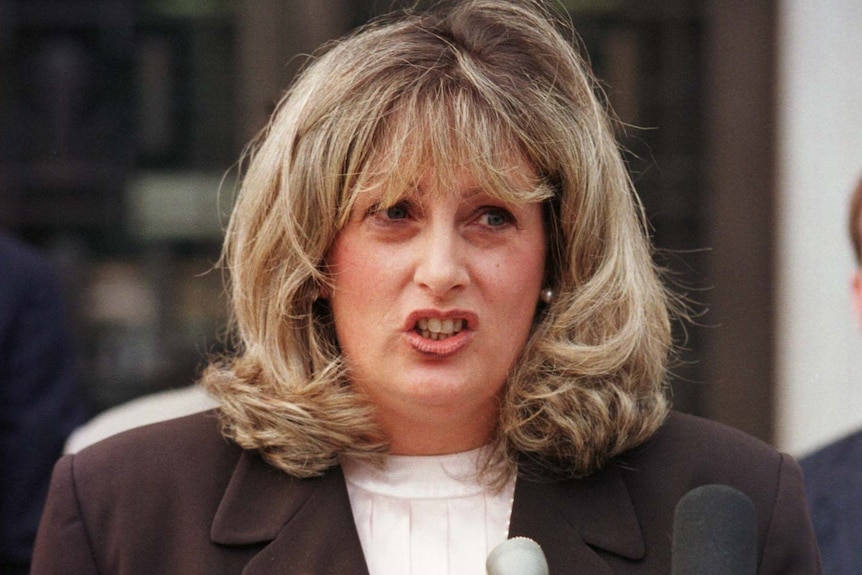 Linda Tripp speaks in front of a dozen microphones.