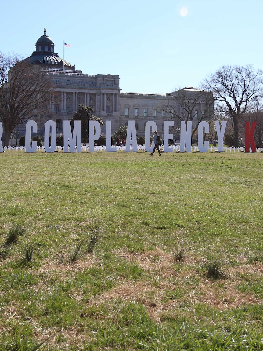 Giant red and white letters spelling out "Your Complacency Kills Us" stand across from the US capitol