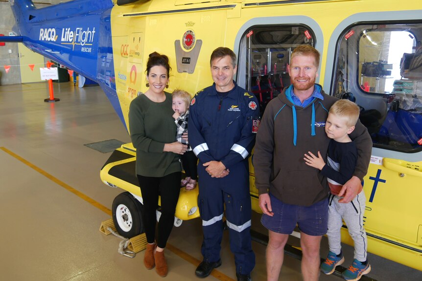 A man with his wife and kids and a paramedic standing in front of a rescue helicopter