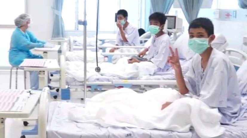 Three of the 12 boys are seen recovering in their hospital beds.