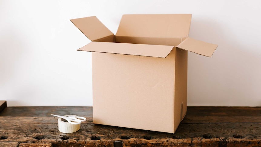 An empty cardboard moving box sitting beside a pair of scissors and a roll of tape