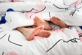 Two pairs of feet stick out from under a doona.