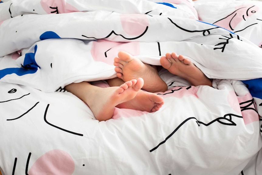 Two pairs of feet stick out from under a doona.