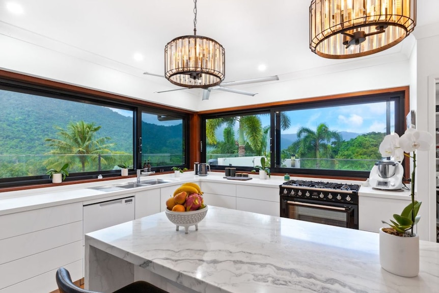 Modern kitchen with stone benchtop, fancy light fittings, ceiling fan and low-line windows overlooking a densely treed valley