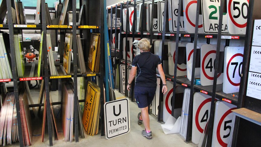 A woman walks past shelves full of road speed and traffic signs
