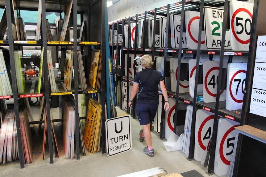 A woman walks past shelves full of road speed and traffic signs