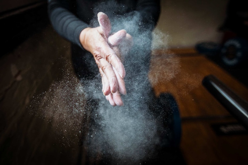 Two hands rubbing together with white chalk dust in a cloud in the air.
