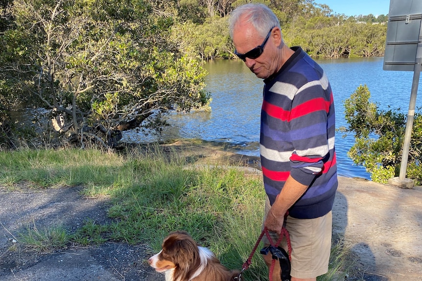 A man in a stripey jumper walks his dog next to a walk