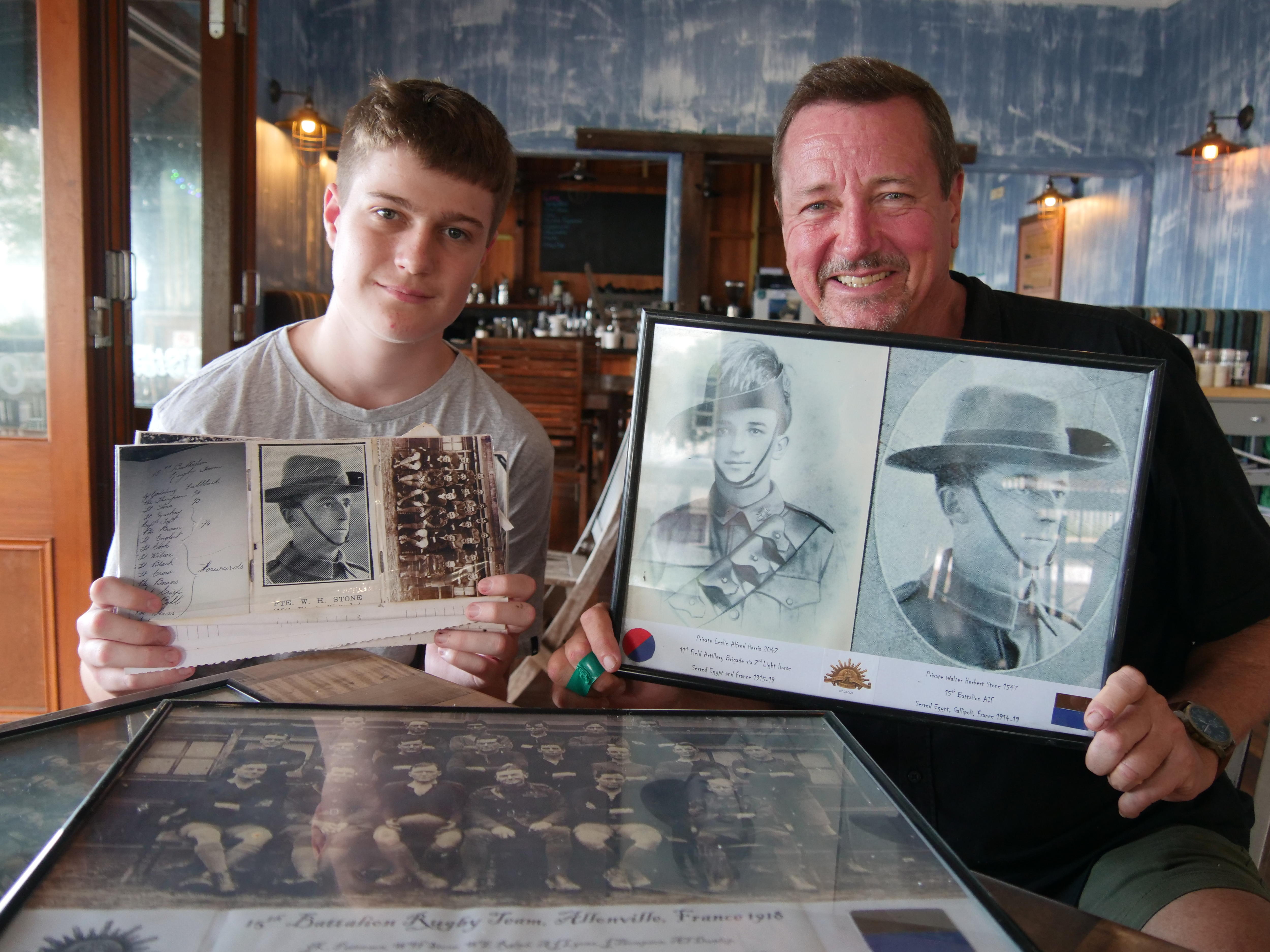 Two males sitting at table holding up photos