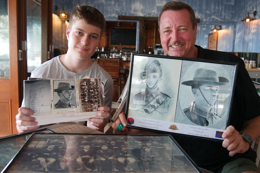 Two males sitting at table holding up photos