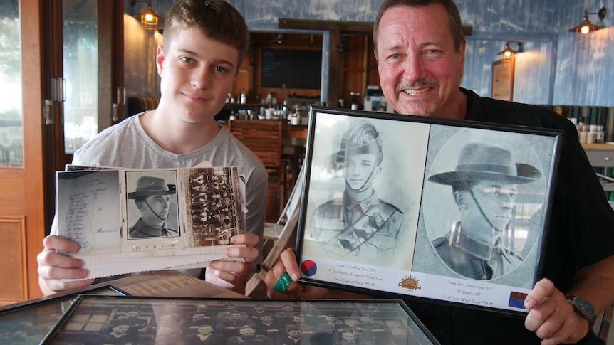 Two males sitting at table holding up photos