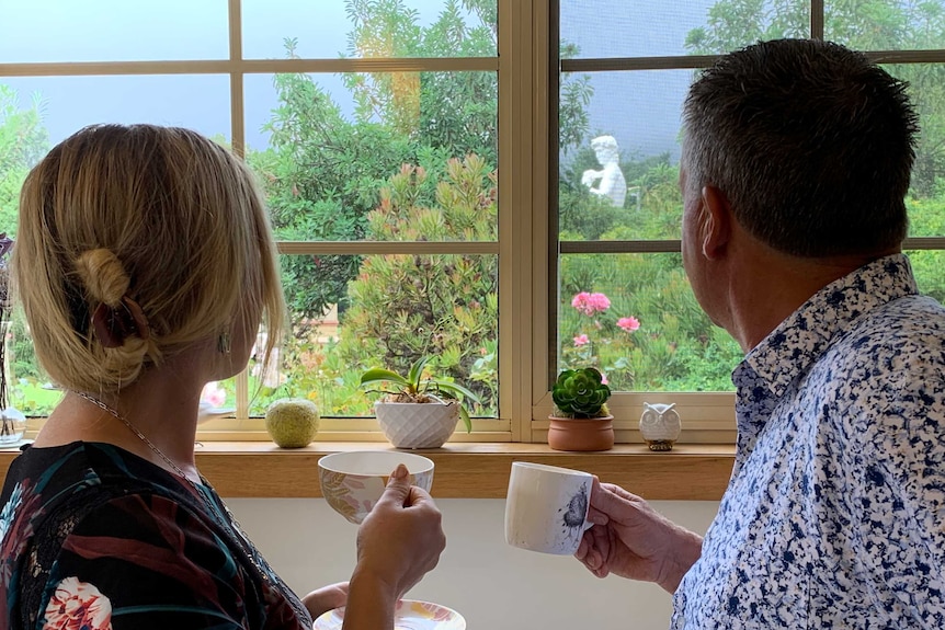 Two people look out of a window at a David statue replica in their backyard