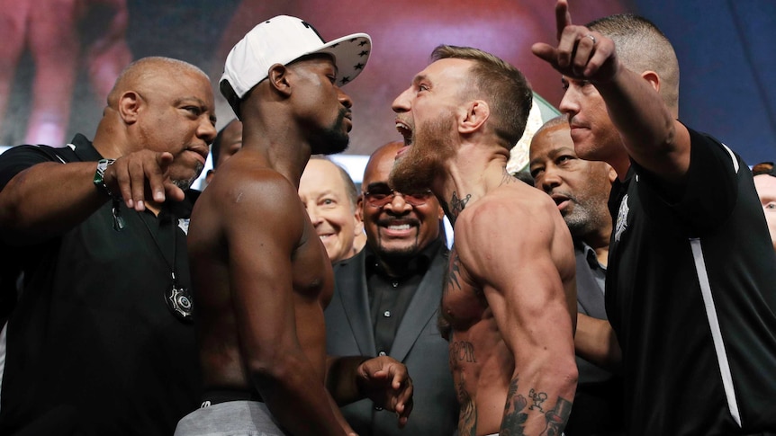 Shirtless Conor McGregor screams in the face of Floyd Mayweather while surrounded by their handlers.