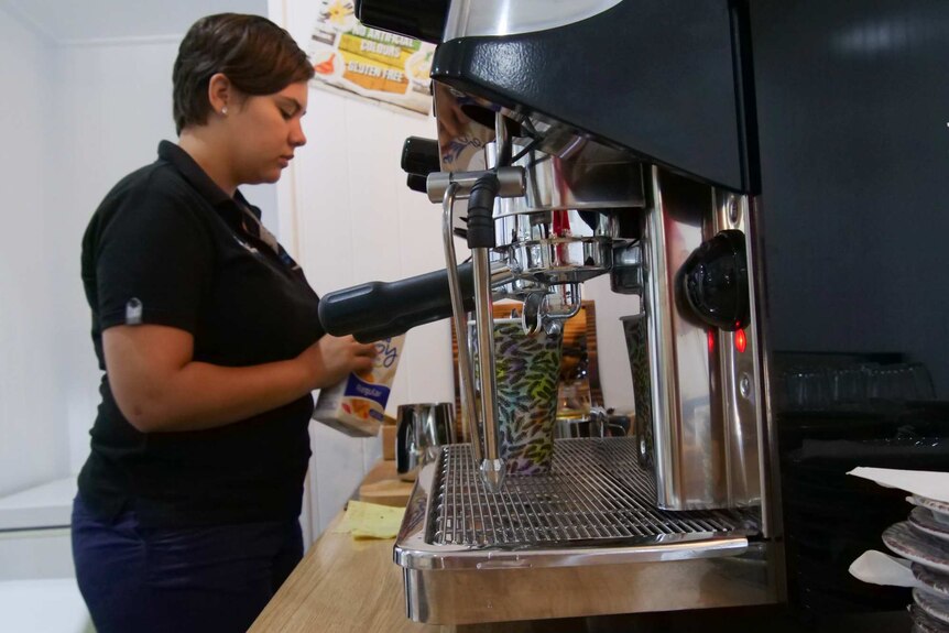 A barista stands making a coffee at a coffee machine.