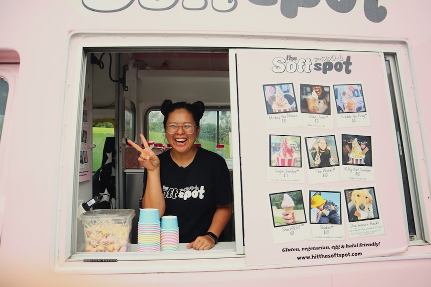 Woman standing inside and ice cream truck holding up a peace sign.