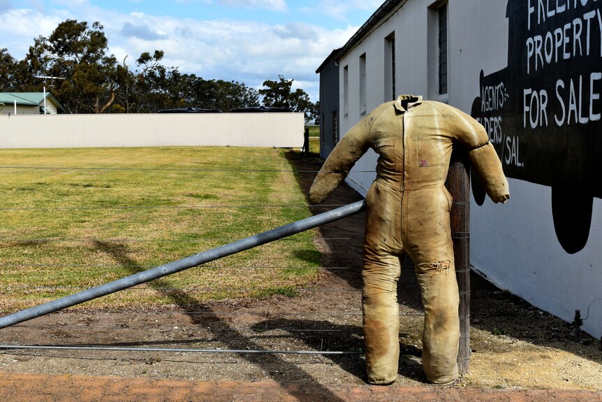 A sculpture of a straw stuffed person leaning against a fence