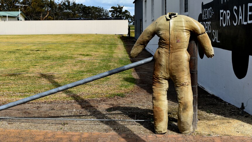 A sculpture of a straw stuffed person leaning against a fence