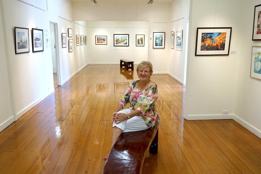 Elaine Madill sits in the middle of an art gallery space surrounded by paintings