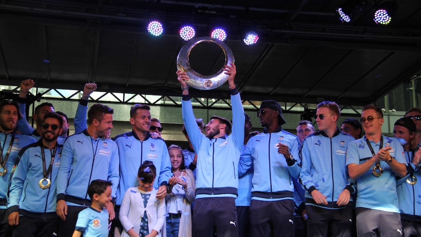 Sydney FC players celebrate with the A-League trophy on stage at Pitt Street mall on May 8, 2017.