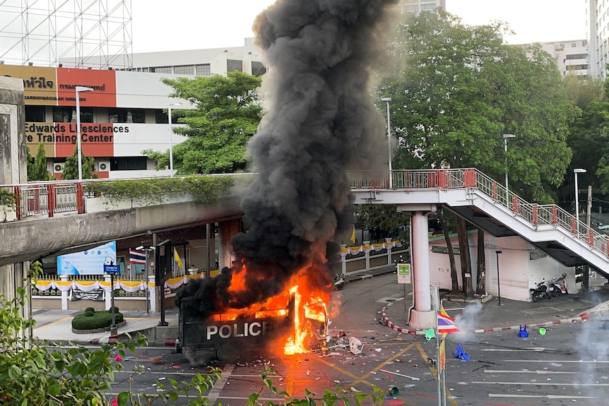 A police truck spews flames and thick grey smoke in the middle of an empty intersection