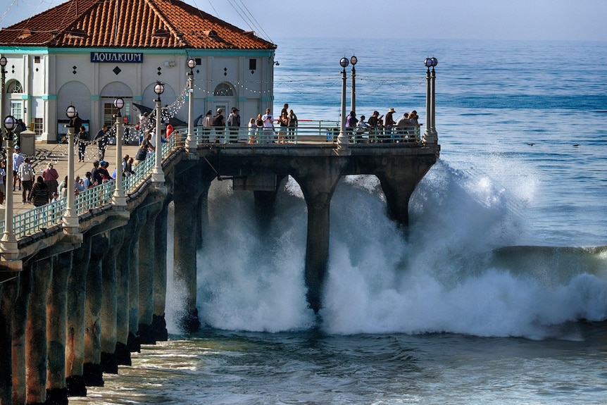 La gente osserva le onde turbolente che si infrangono lungo il molo di Manhattan Beach, in California