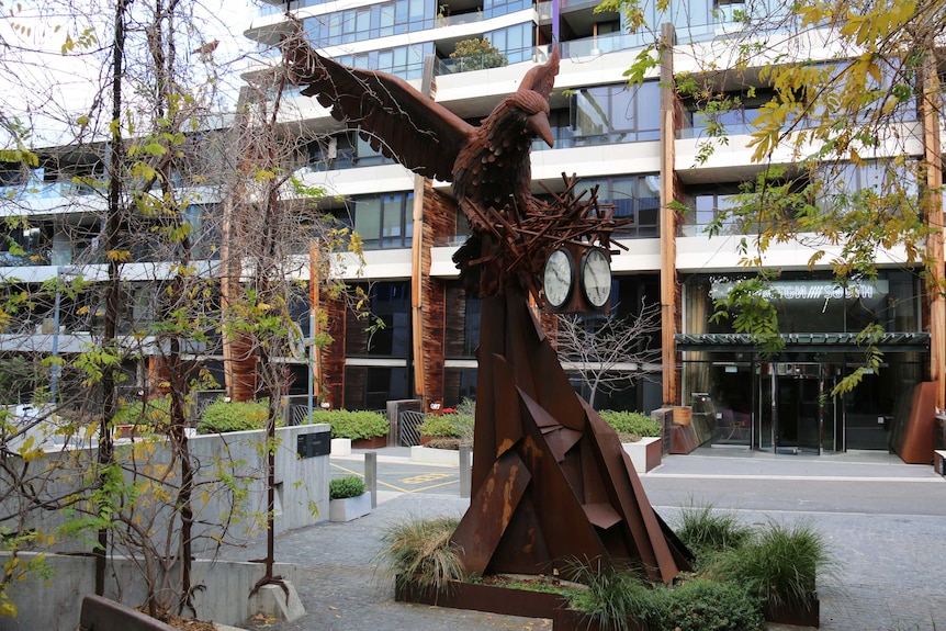 A metal sculpture of a bird with a nest of clocks.