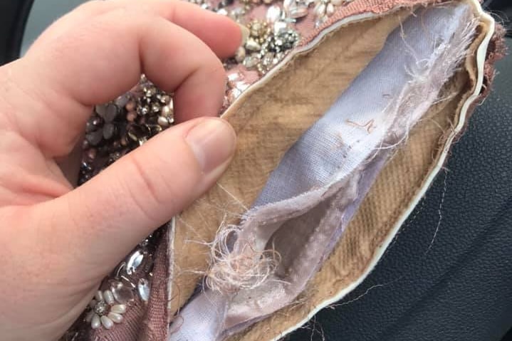 A hand holds a small fabric purse that has been torn apart.