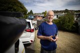 A middle aged man wearing a blue tshirt holds an electric car charger in a suburban driveway