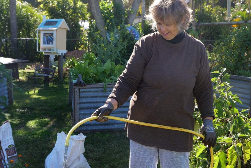 Berni Jakstas, woman watering the community garden, smiling.