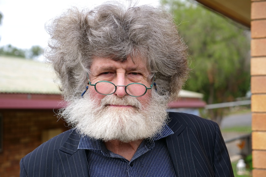 Garry, a man with long dark and light grey hair, white beard, round glasses looking at the camera. 