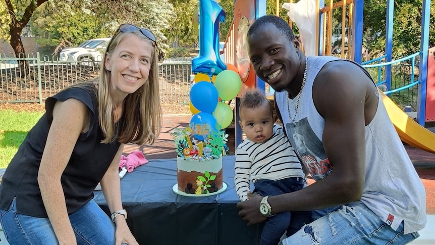 A woman and a man holding a toddler in front of a playground