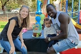 A woman and a man holding a toddler in front of a playground
