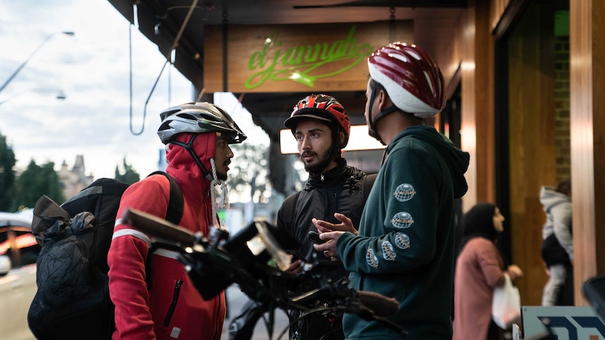 Three cyclists wearing helmets stand outside a restaurant.