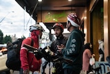 Three cyclists wearing helmets stand outside a restaurant.