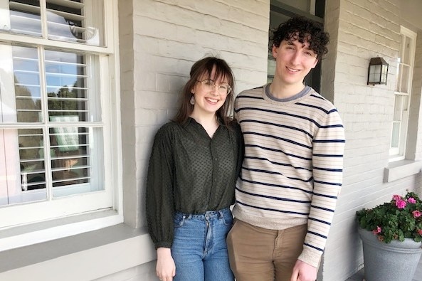 A young man and woman stand in front of their house