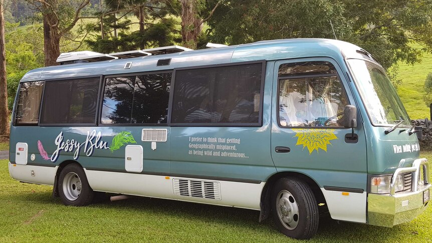 A aqua green and white minibus converted into a motorhome parked on grass in the bush