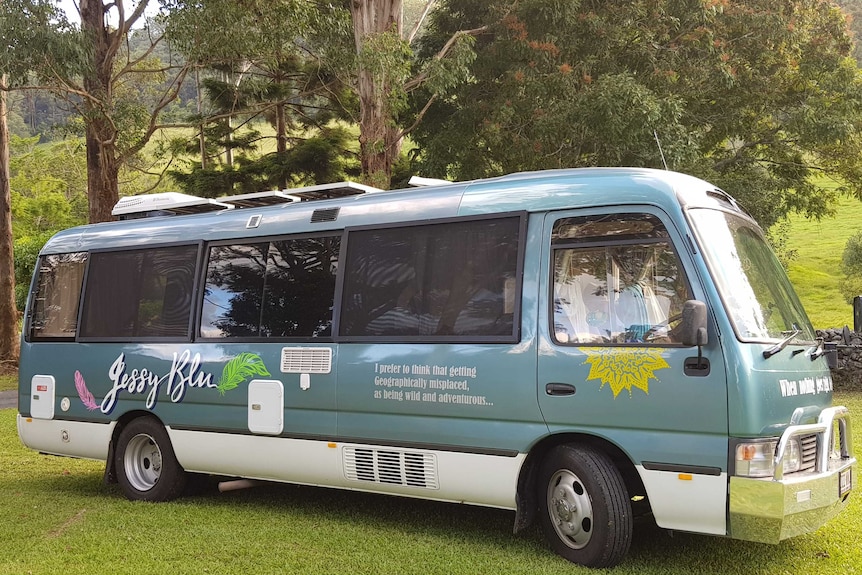 A aqua green and white minibus converted into a motorhome parked on grass in the bush