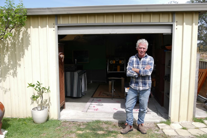 He stands in his backyard by his shed