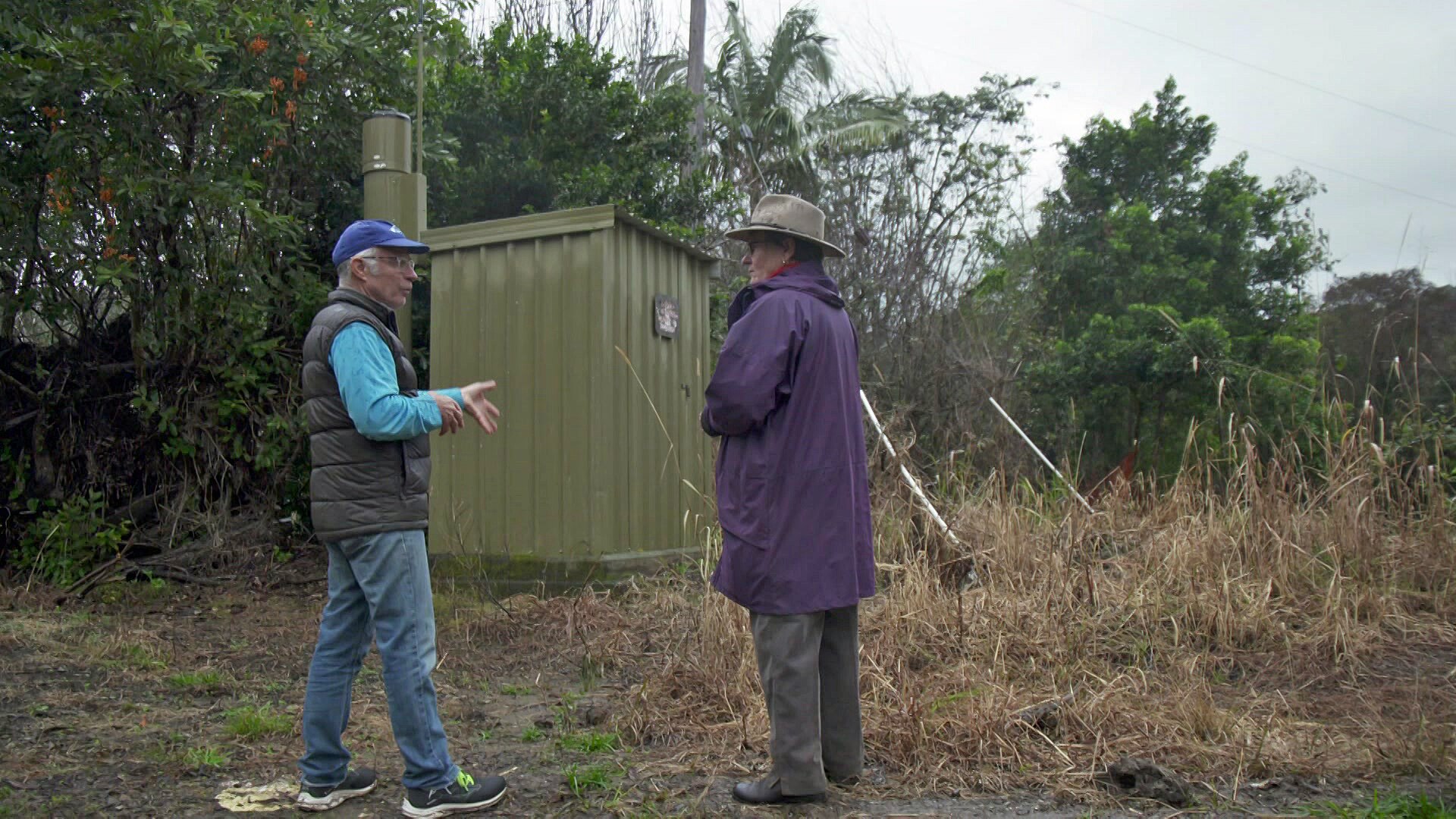 A man and woman stand next to a rain gauge which looks like a green shed.
