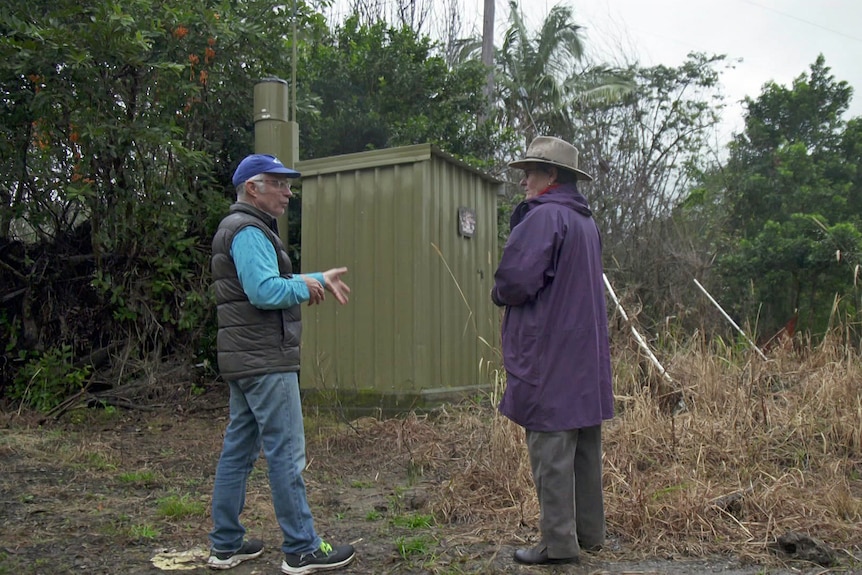 A man and woman stand next to a rain gauge which looks like a green shed.