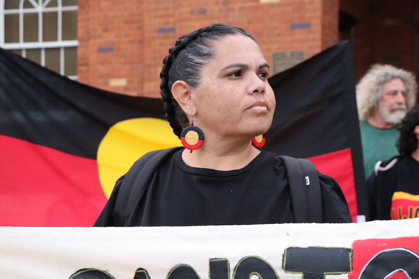 Woman wears Aboriginal flag earrings, with an Aboriginal flag behind her.