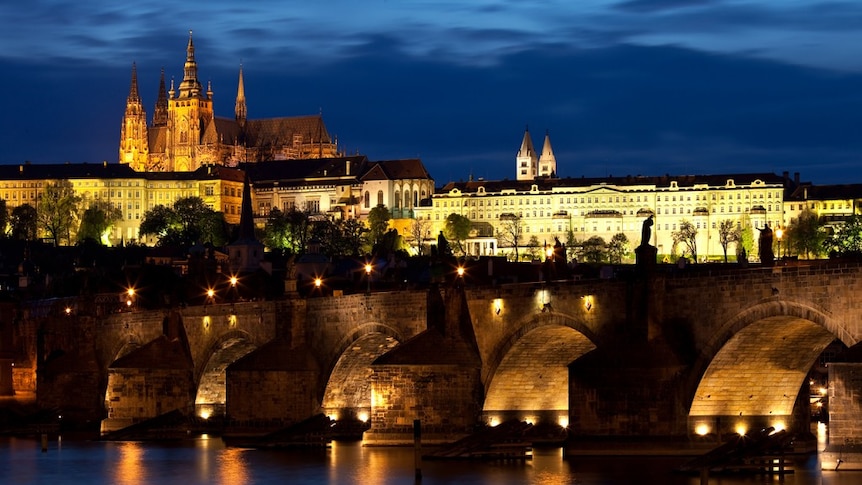 Prague's bustling Charles Bridge by night, with a view up to the city's expansive castle complex. (Wikimedia Commons)