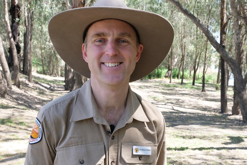 A man in Khaki shirt and wide brimmed hat smiles at the camera