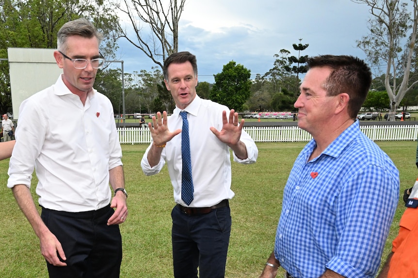 three men standing outdoors, one is wearing glasses 