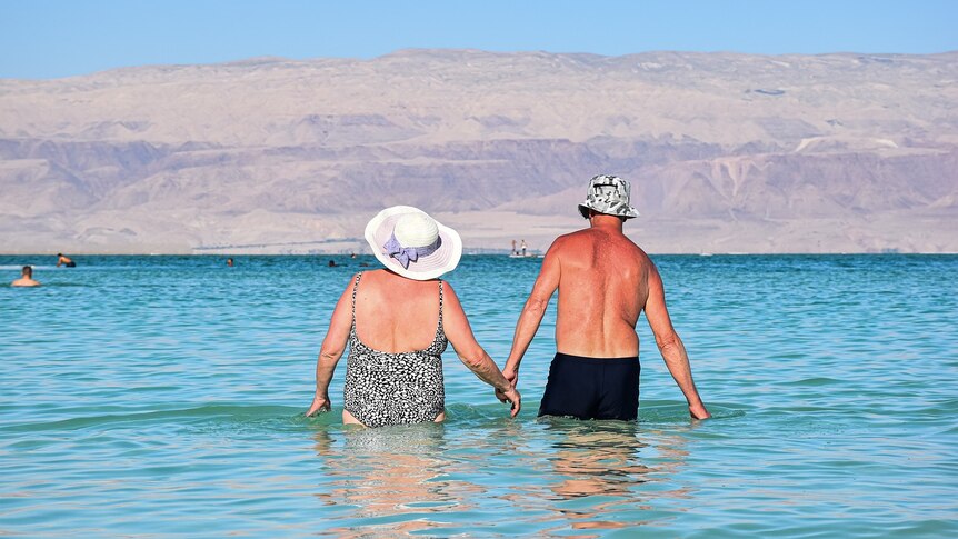 Elderly couple holding hands in the water in their bathers.
