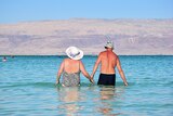 Elderly couple holding hands in the water in their bathers.